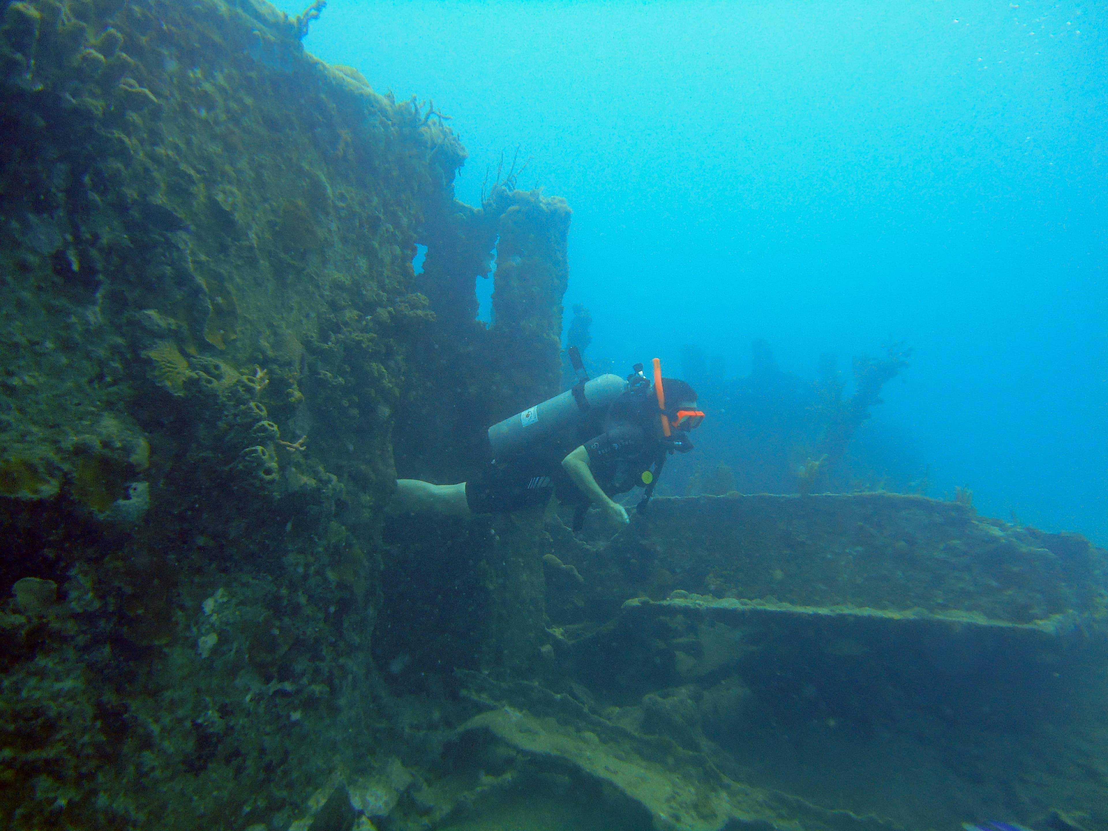 Scuba diver exploring sunken shipwreck covered in coral and marine life